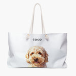 Watercolor portrait of an apricot doodle dog on a soft white weekender bag with white rope handles, with the name COCO printed above.