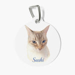 Round white pet tag on a metal clasp, printed with a softly shaded colored-pencil portrait of a pale tabby cat with blue eyes, named Sushi.