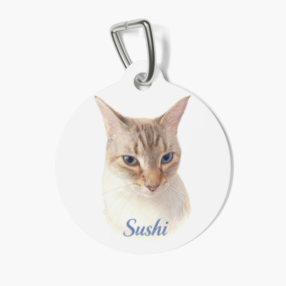 Round white pet tag on a metal clasp, printed with a softly shaded colored-pencil portrait of a pale tabby cat with blue eyes, named Sushi.