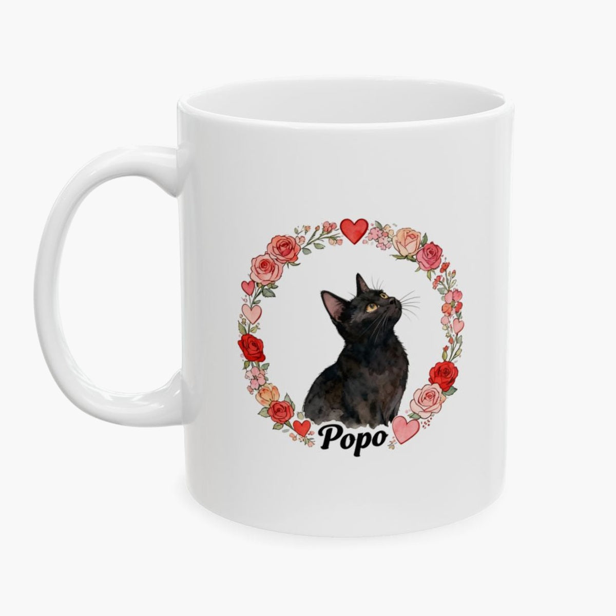 Black cat looking upward inside a wreath of roses and hearts on a white mug, with the name Popo in black script below.