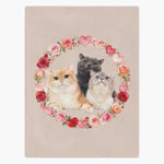 Beige fleece blanket printed with three cats, one ginger, one gray and one cream, framed by a ring of watercolor roses and hearts.
