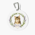 Round white pet tag on a metal clasp, printed with a watercolor tabby cat inside a rosemary and lavender wreath above a heart reading Smokey.