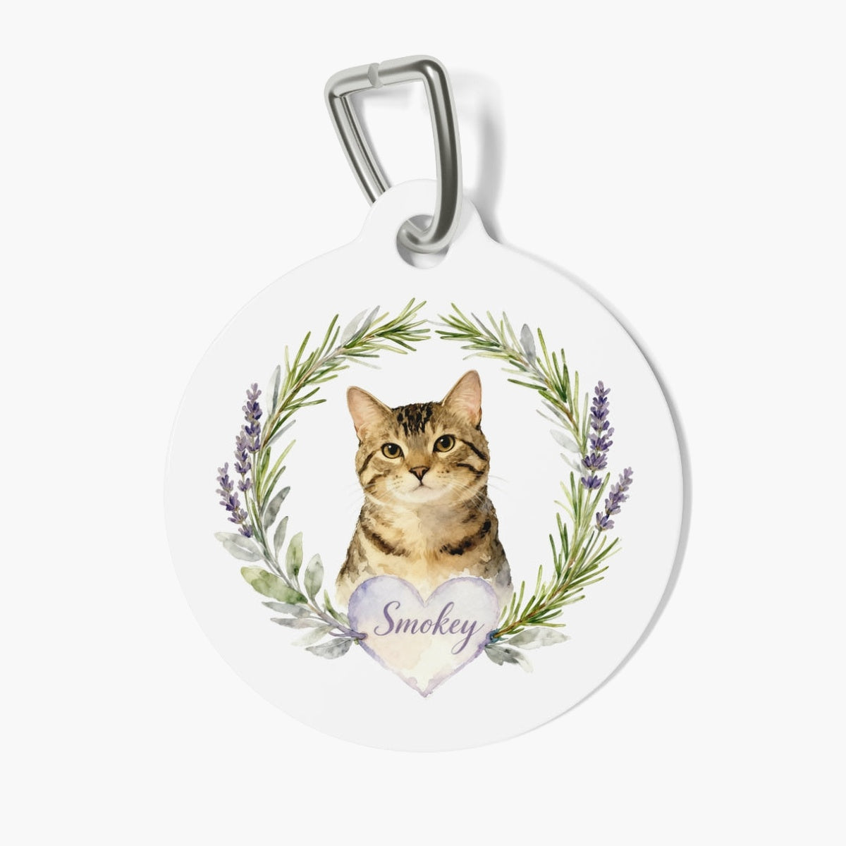 Round white pet tag on a metal clasp, printed with a watercolor tabby cat inside a rosemary and lavender wreath above a heart reading Smokey.