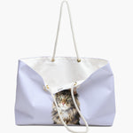 The lavender weekender bag standing open, white cotton lining and care label showing, with the watercolor Maine Coon portrait below.