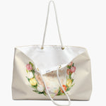The cream tulip-wreath weekender bag standing open, white lining and care label showing, with the Persian cat and its name heart below.