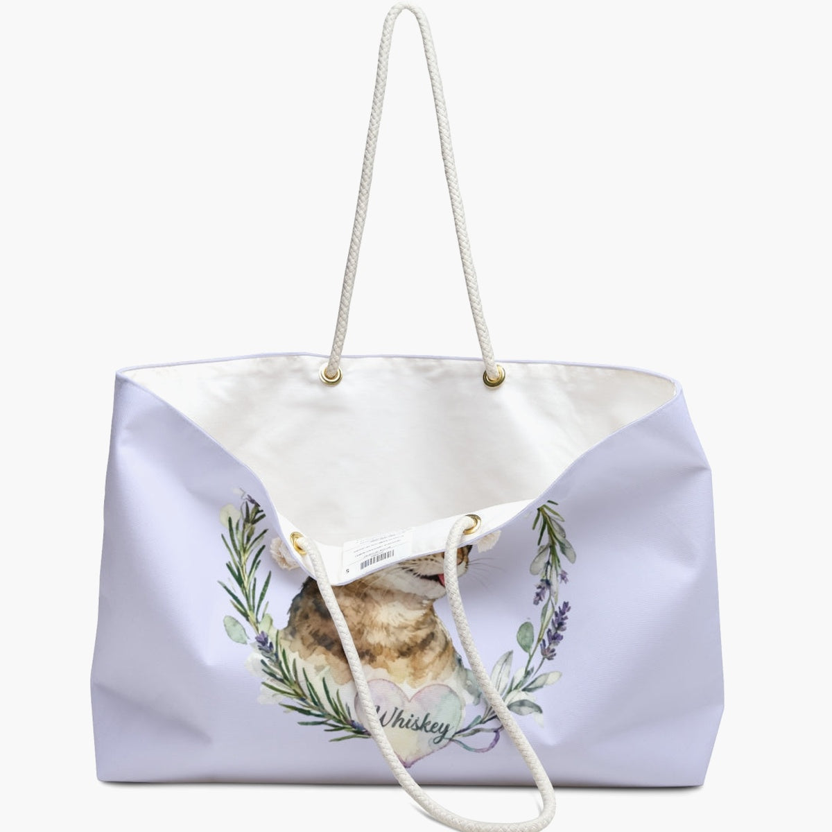 The lilac herb-wreath weekender bag standing open, white lining and care label showing, with the tabby cat and "Whiskey" heart below.