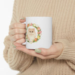 Hands in a beige knit sweater holding the white mug, showing the cream Persian cat framed by a watercolor tulip wreath.