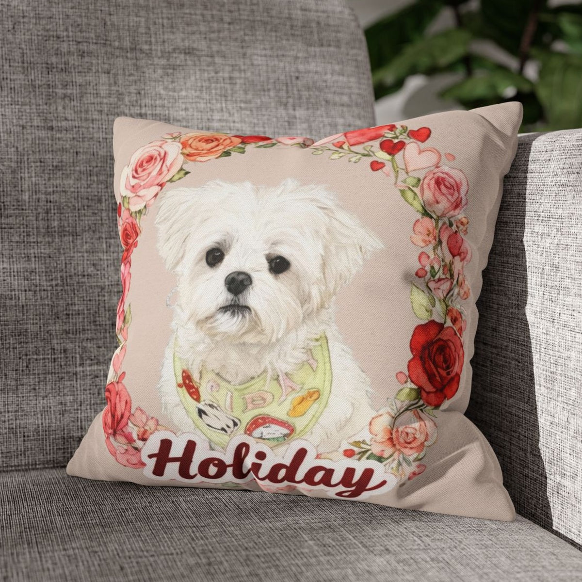 The beige rose-wreath pillow showing a white Maltese in a patterned bib and the name "Holiday", propped on a gray woven couch.