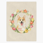 Cream fleece blanket printed with a smiling corgi framed by a ring of watercolor tulips, the pet's name in a pink heart below.