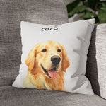 The soft white pillow with the golden retriever "COCO" design, propped in the corner of a gray woven couch beside a leafy houseplant.