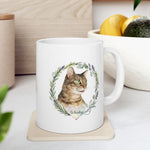 The mug on a kitchen counter beside a bowl of lemons and an avocado, showing the tabby cat in a rosemary and lavender wreath.