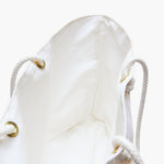 Close-up inside the weekender bag showing the white cotton lining, gold-tone grommets and knotted white rope handles.