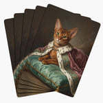 Five cards fanned face down, each back a painted portrait of a ginger cat in an ermine-trimmed pink robe and pearl necklace on a teal cushion.