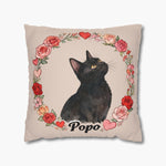 Watercolor black cat looking upward inside a wreath of roses and hearts on a beige throw pillow, with the name "Popo" printed below.