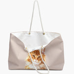 The dusty pink weekender bag standing open, white cotton lining and care label visible, with the watercolor ginger cat portrait below.