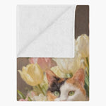 Folded corner of the blanket showing its plain white fleece backing, with the calico cat and tulip painting on the printed side.