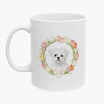 Watercolor portrait of a fluffy white Maltese inside a pastel tulip wreath on a white mug, with the pet's name lettered on a heart below.