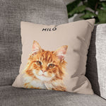 The dusty pink pillow with the ginger cat "MILO" design, resting in the corner of a gray woven couch with a green houseplant behind it.