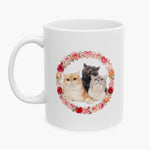 Three cats, one ginger, one gray and one cream, grouped inside a wreath of roses and hearts on a white mug, with no name printed.