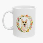 Watercolor portrait of a smiling corgi inside a pastel tulip wreath on a white mug, with the name Raine on a heart below.