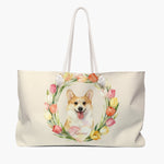 Cream weekender bag printed with a watercolor tulip wreath around a grinning Pembroke Welsh corgi, with "Rainie" in script on a pink heart.