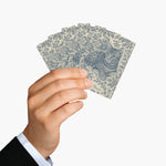 A hand in a dark suit cuff holds five cards fanned backs out, each printed with the blue tabby cat toile design and the name Beans.