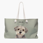 Watercolor portrait of a scruffy gray and cream terrier on a sage weekender bag with white rope handles, with the name JOJO printed above.