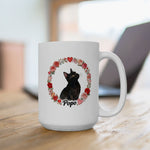 The larger mug on a wooden desk in front of a laptop, showing the black cat Popo inside a wreath of roses and hearts.