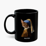 A ginger cat painted into Vermeer's "Girl with a Pearl Earring", in a blue and gold turban with a pearl drop, on an all-black mug, name "DALTON" below.