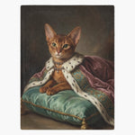 Fleece blanket printed with an oil-painting portrait of a ginger Abyssinian cat in an ermine robe and jeweled necklace on a green cushion.