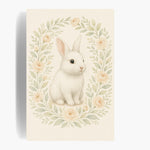 Unframed watercolor print of a white rabbit inside an oval wreath of cream roses and sage leaves on ivory paper.