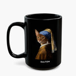 A ginger cat painted into Vermeer's "Girl with a Pearl Earring", in a blue and gold turban with a pearl drop, on a taller all-black mug, name "DALTON" below.
