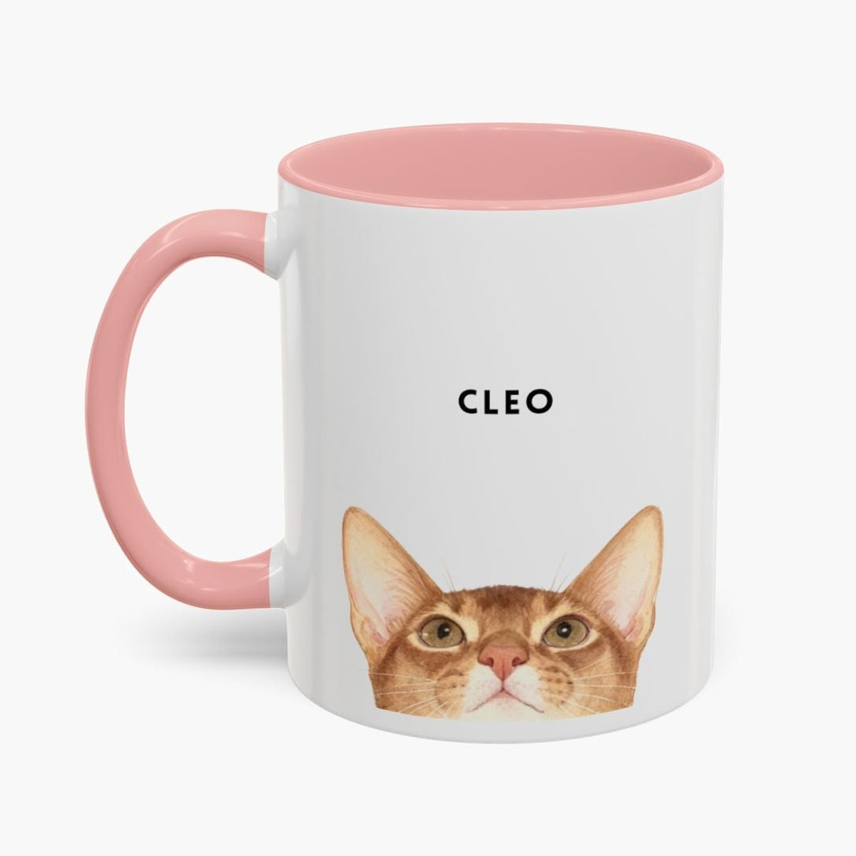 Watercolor ginger cat peeking up over the bottom edge of a white 11 oz mug with a pink handle and inner glaze, name "CLEO" above.