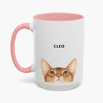 Watercolor ginger cat peeking up over the bottom edge of a taller white 15 oz mug with a pink handle and inner glaze, name "CLEO" above.